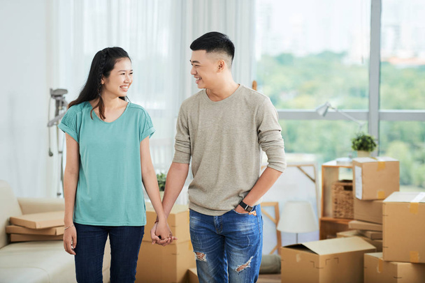 Onnellinen aasialainen pari seisoo kädestä ja hymyilee toisilleen muuttaessaan uuteen taloon.
 - Valokuva, kuva