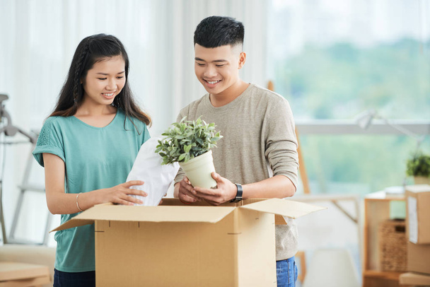 Usměvavý asijský párek stojící blízko lepenkové krabice a vybalování v novém domě - Fotografie, Obrázek