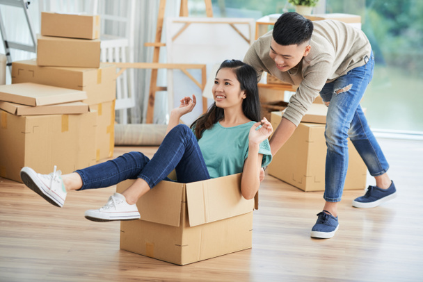 Asian young man playing with his girlfriend while she sitting in big cardboard box they having fun at home - Photo, Image