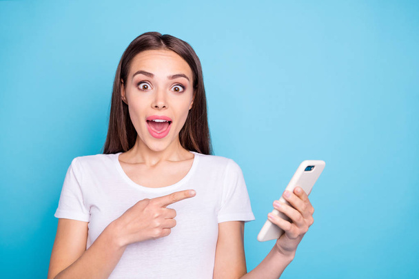 Portrait of impressed millennial hold modern technology point information scream wow omg wear white t-stylish t-shirt isolated over blue background - 写真・画像