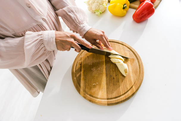 cropped view of pregnant woman cutting banana on chopping board  - Фото, зображення