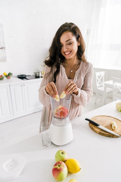 happy pregnant woman putting banana in blender with grapefruit  - Foto, afbeelding