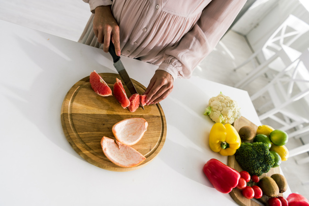 overhead view of young pregnant woman cutting grapefruit  - Fotografie, Obrázek