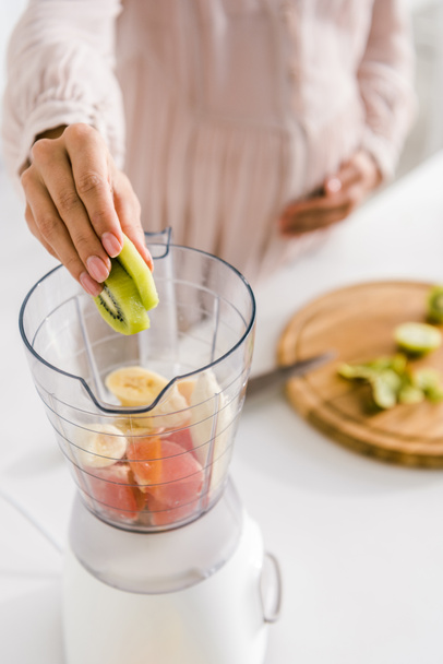 selective focus of pregnant woman putting kiwi into blender  - Photo, Image