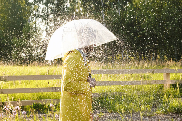 Yağmurda sarı yağmurluk giyen bir adam. Yağmur yağıyor ve güneş parlıyor..  - Fotoğraf, Görsel