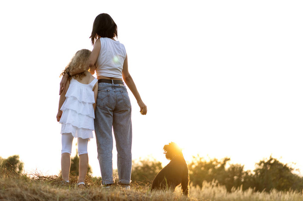 Μητέρα με κόρη με σκυλί μινιατούρα σνάουζερ παίζει στο ηλιοβασίλεμα - Φωτογραφία, εικόνα