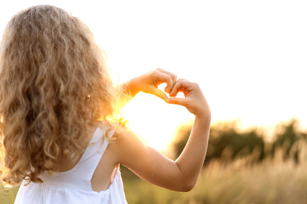 klein meisje bij zonsondergang toont een hart met handen speelt in het veld - Foto, afbeelding