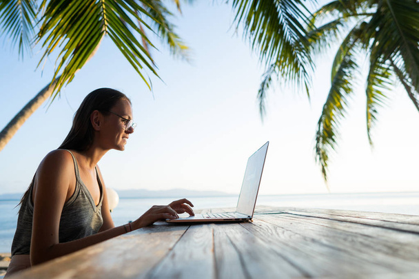 freelancer dziewczyna z komputerem wśród tropikalnych palm pracy na wyspie o zachodzie słońca - Zdjęcie, obraz