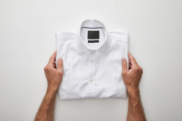 cropped view of man holding folded shirt on white background - Fotó, kép