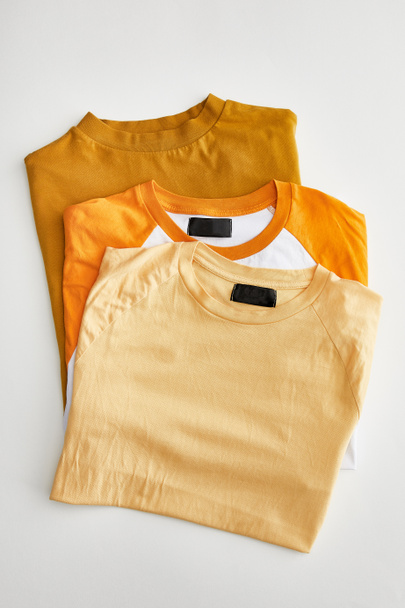 top view of beige, orange and ochre folded t-shirts on white background - Fotó, kép