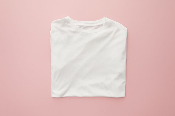 Draufsicht auf leeres weißes gefaltetes T-Shirt auf rosa Hintergrund - Foto, Bild