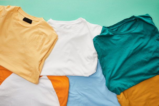 vista superior de las camisetas plegadas de color naranja, beige, blanco, azul y ocre sobre fondo turquesa
 - Foto, imagen