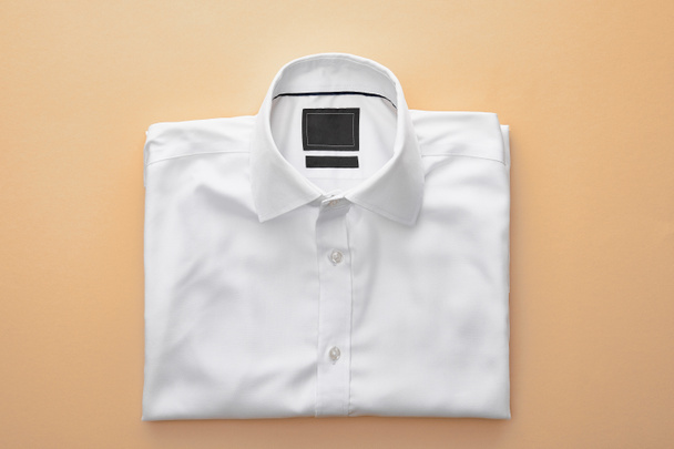 top view of plain white folded shirt on beige background - Fotografie, Obrázek
