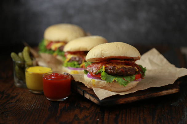 Wołowina burger w ciemnym tonie z niskim kluczem światła na drewnianej płycie i ciemnym tle - Zdjęcie, obraz