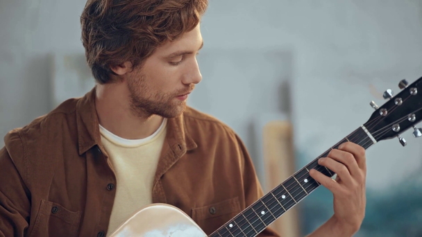 νέος κοκκινομάλλης άνθρωπος παίζει ακουστική κιθάρα στο σπίτι - Πλάνα, βίντεο