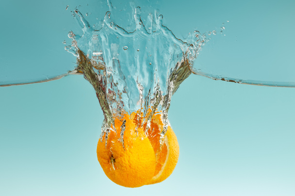 ripe orange halves falling in water with splashes on blue background - Foto, afbeelding