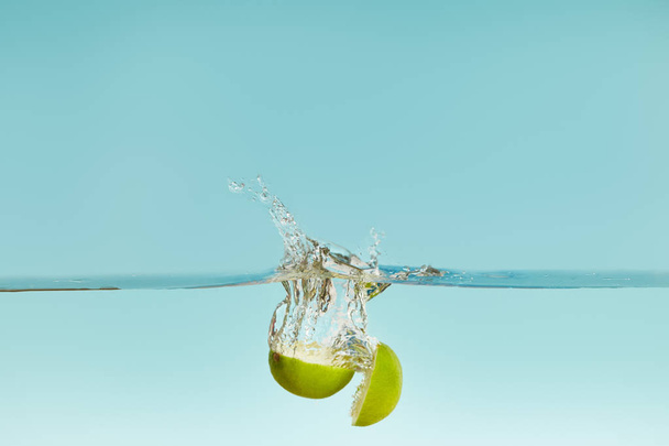 ripe lime halves falling in water with splash on blue background - Photo, image