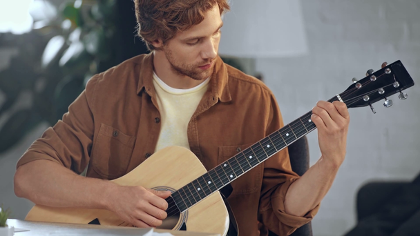 κοκκινομάλλα άνθρωπος παίζει ακουστική κιθάρα στο σπίτι - Πλάνα, βίντεο