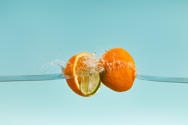 ripe orange halves falling in water with drops on blue background - Fotoğraf, Görsel