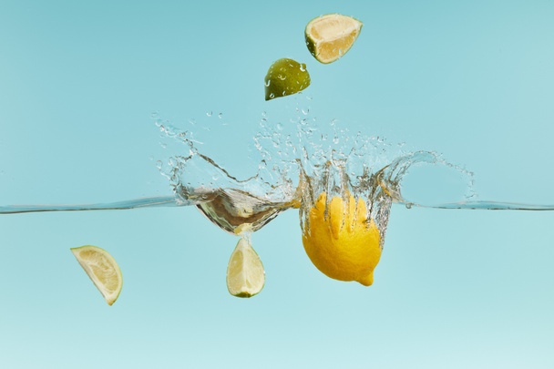 ripe lemon and lime pieces falling deep in water with splash on blue background - Photo, Image