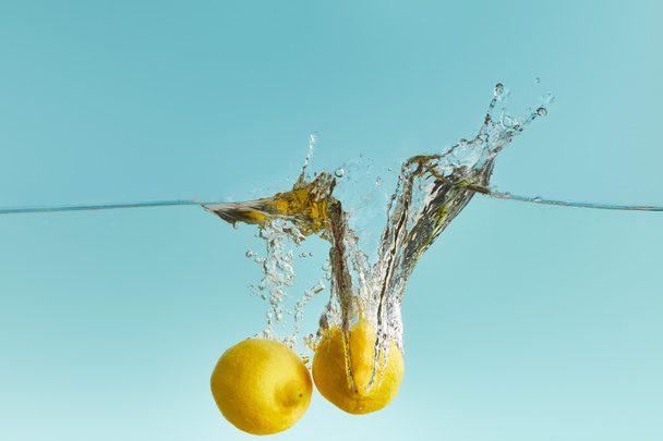 citrons mûrs entiers tombant profondément dans l'eau avec éclaboussure sur fond bleu
 - Photo, image