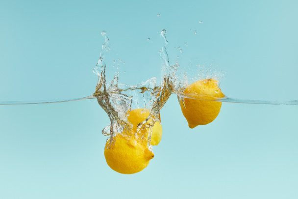 lemons falling deep in water with splash on blue background - Photo, Image
