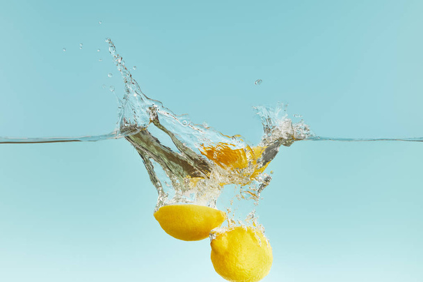 gele citroenen die diep in watervallen met Splash op blauwe achtergrond - Foto, afbeelding