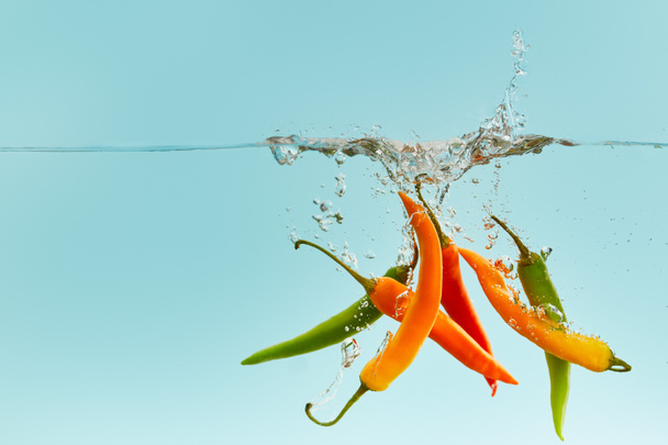 colorful chili peppers falling deep in water with splash on blue background - Foto, imagen