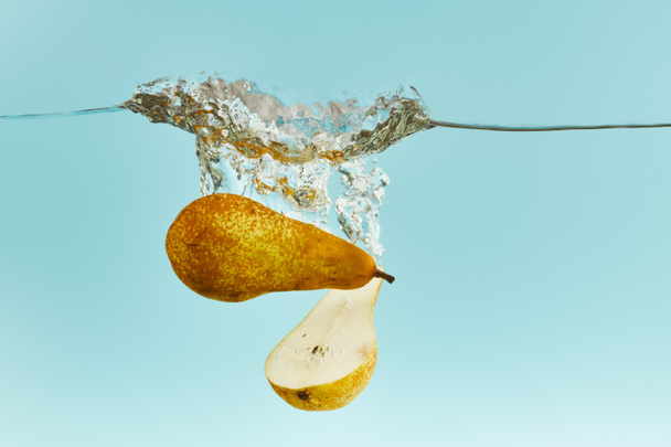 cut pear falling deep in water with splash on blue background - Foto, afbeelding