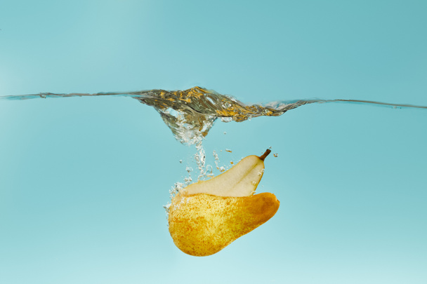 ripe pear halves falling deep in water with splash on blue background - Fotó, kép