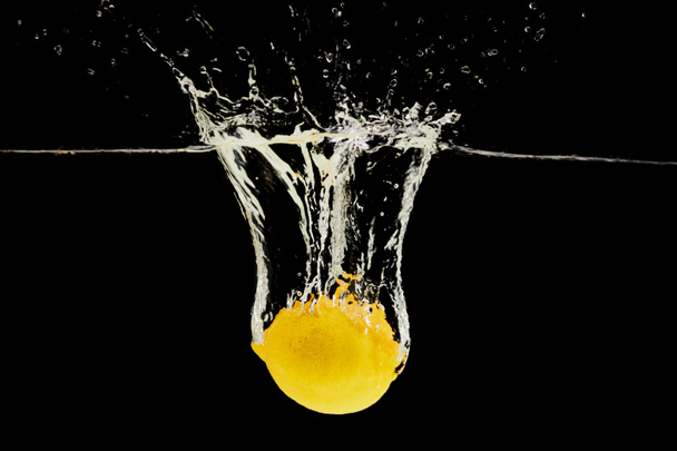 reife Zitrone fällt tief ins Wasser mit Spritzer isoliert auf schwarz - Foto, Bild