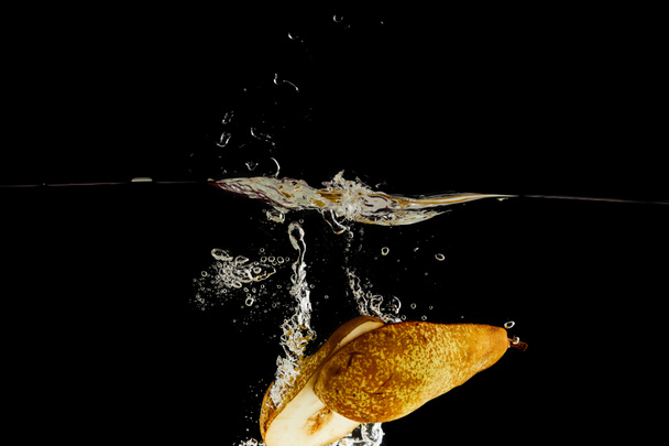 dojrzałych połówki gruszy opadających głęboko w wodzie z rozpryskami na czarno - Zdjęcie, obraz