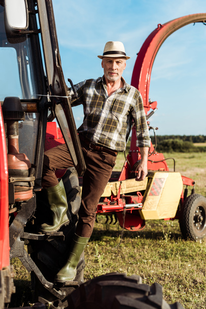 granjero senior autónomo mirando la cámara cerca del tractor moderno
  - Foto, Imagen