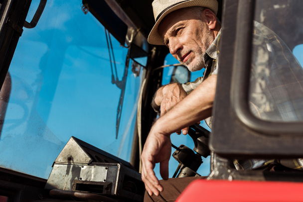 vista de ángulo bajo del agricultor senior tocando el volante en el tractor
  - Foto, Imagen