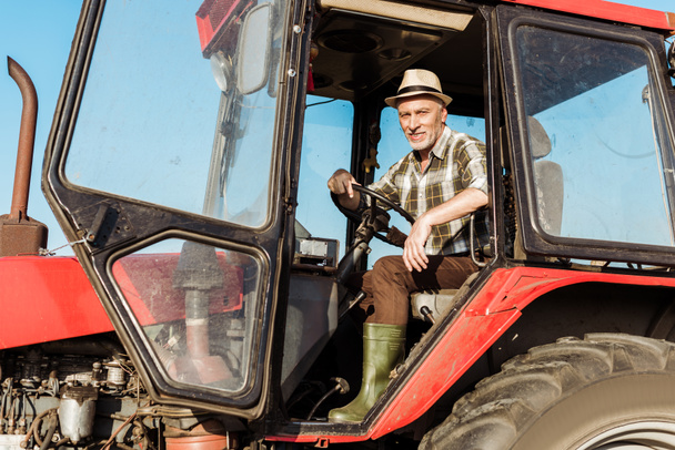 happy senior self-employed farmer in straw hat driving tractor  - Photo, Image