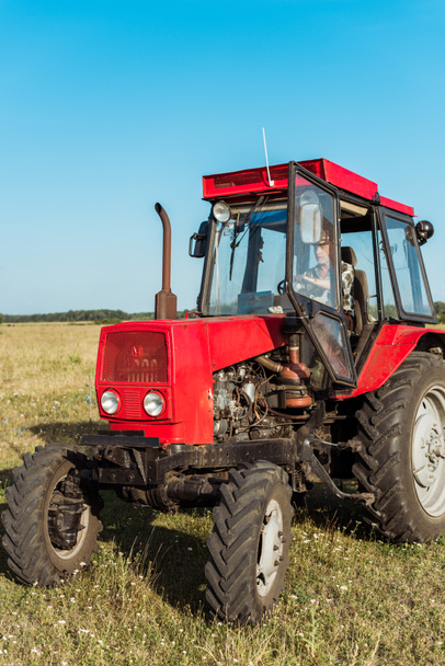 agriculteur âgé conduisant tracteur rouge dans le champ de blé
  - Photo, image