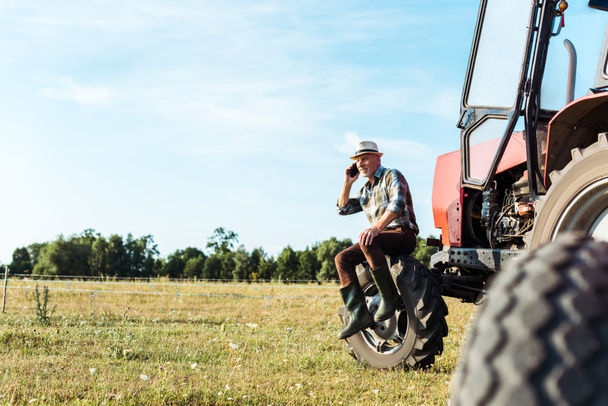enfoque selectivo de agrónomo hablando en el teléfono inteligente cerca del tractor
  - Foto, Imagen