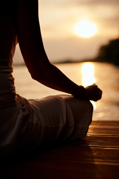 Vista posteriore della donna caucasica seduta in posizione di loto e meditando sul molo al tramonto
. - Foto, immagini