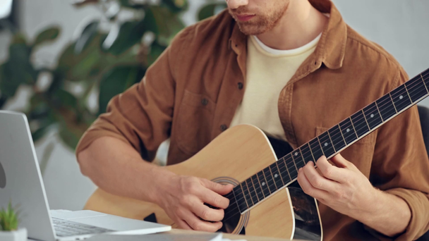 partial view of man playing acoustic guitar and using laptop - Filmagem, Vídeo