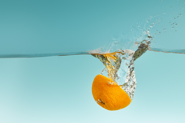 bright orange half falling in water with splash on blue background - Foto, afbeelding