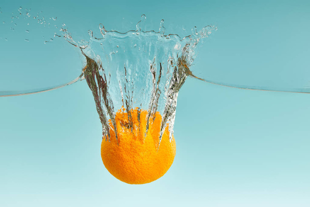 leckere frische Orange fällt in Wasser mit Spritzer auf blauem Hintergrund - Foto, Bild
