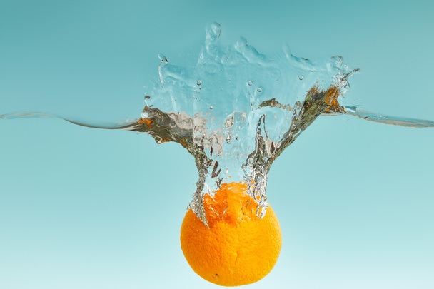 ripe fresh orange falling in water with splash on blue background - Photo, Image