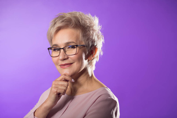 portrait of adult woman in glasses with short haircut on purple background - Foto, imagen