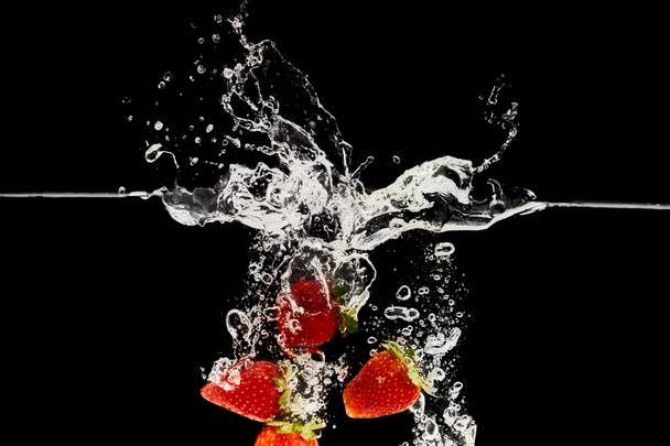 czerwone, dojrzałe truskawki opadające w wodzie z odpryskami na czarno - Zdjęcie, obraz