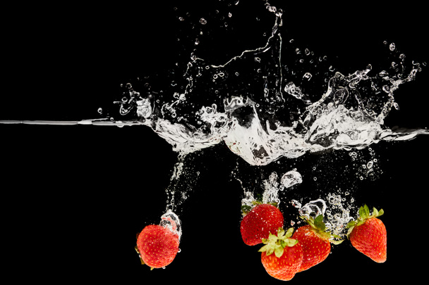fraises fraîches mûres tombant dans l'eau avec éclaboussures isolées sur noir
 - Photo, image