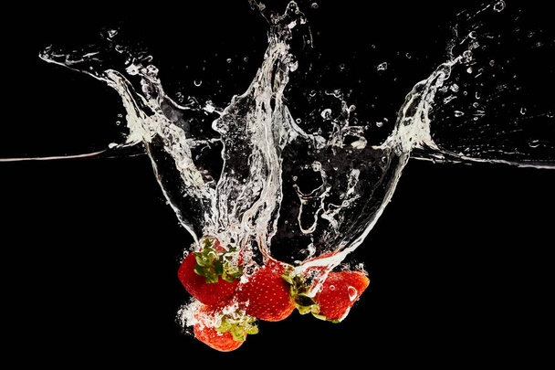 morangos maduros doces caindo na água com respingo isolado no preto
 - Foto, Imagem