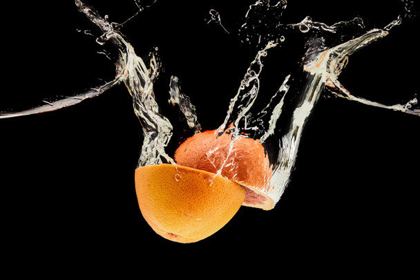 ripe grapefruit halves falling in water with splash isolated on black - Photo, Image