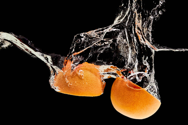 mitades de pomelo orgánico que caen en el agua con salpicaduras aisladas en negro
 - Foto, Imagen