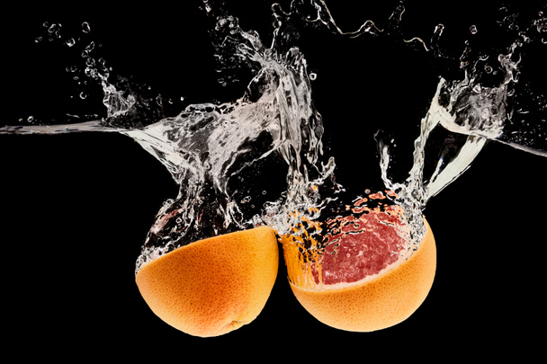 спелый натуральный грейпфрут наполовину падает в воду с брызги изолированы на черный
 - Фото, изображение
