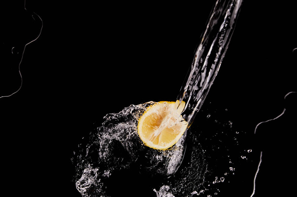Top uitzicht van Lemon half met helder water splash geïsoleerd op zwart - Foto, afbeelding